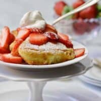 white pedestal plate filled with fluffy French toast, whipped cream and strawberries