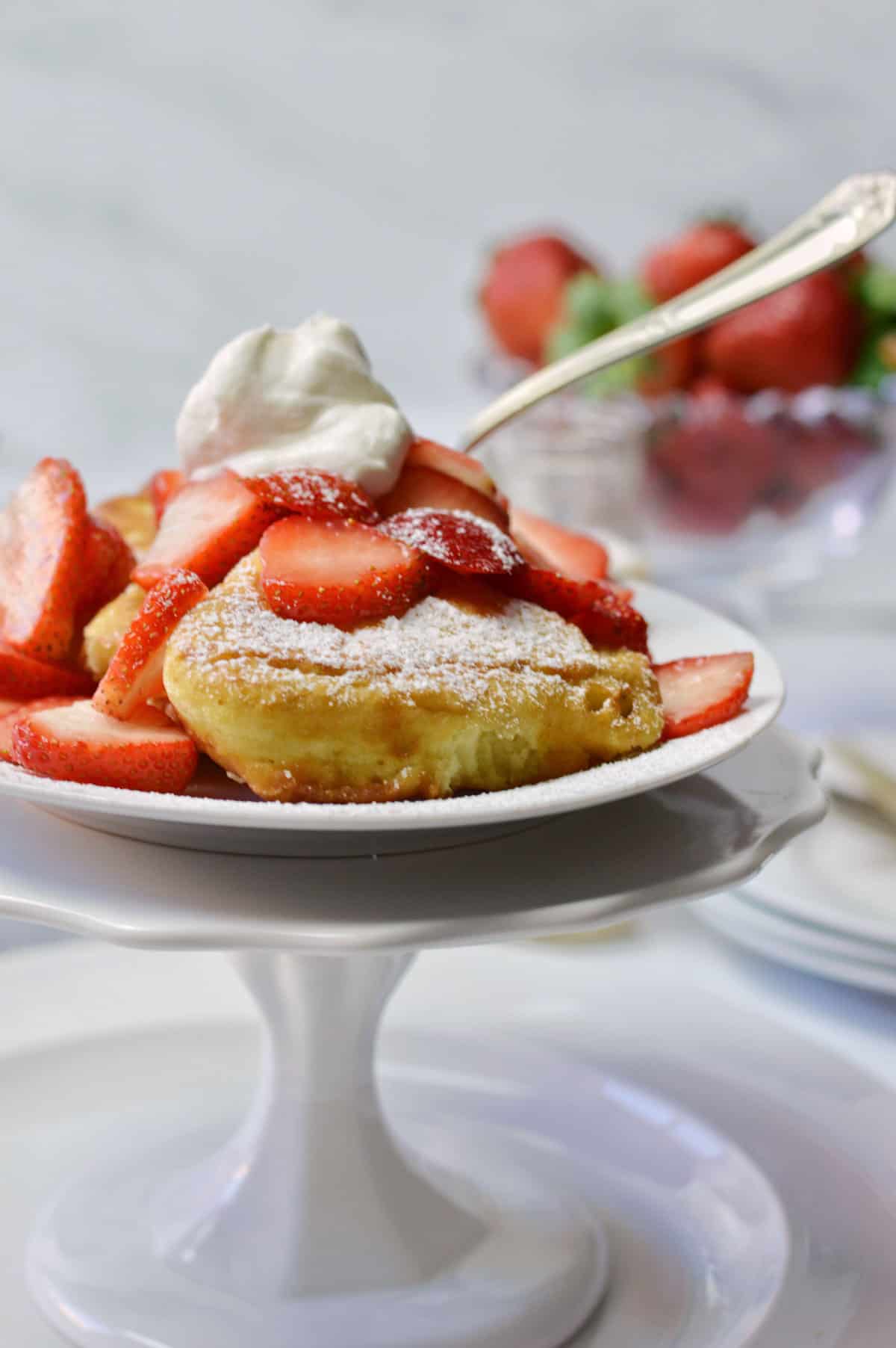 pedestal dish of fluffy French toast with strawberries and cream.