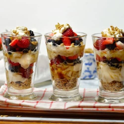 3 layered berry yogurt parfait with granola in clear glasses
