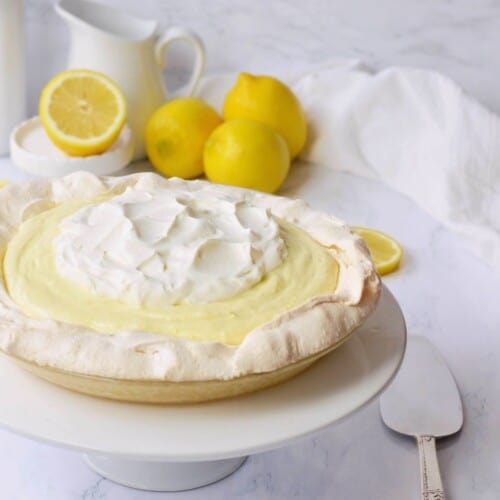 Meringue crust filled with yellow lemon mousse and white whipped cream in front of lemons