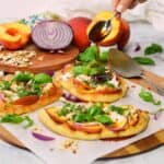 featured image without description. A spoon full of spicy honey vinaigrette pouring over individual flatbread pizzas with Burrata cheese, peaches, red onion, basil and sliced almonds.