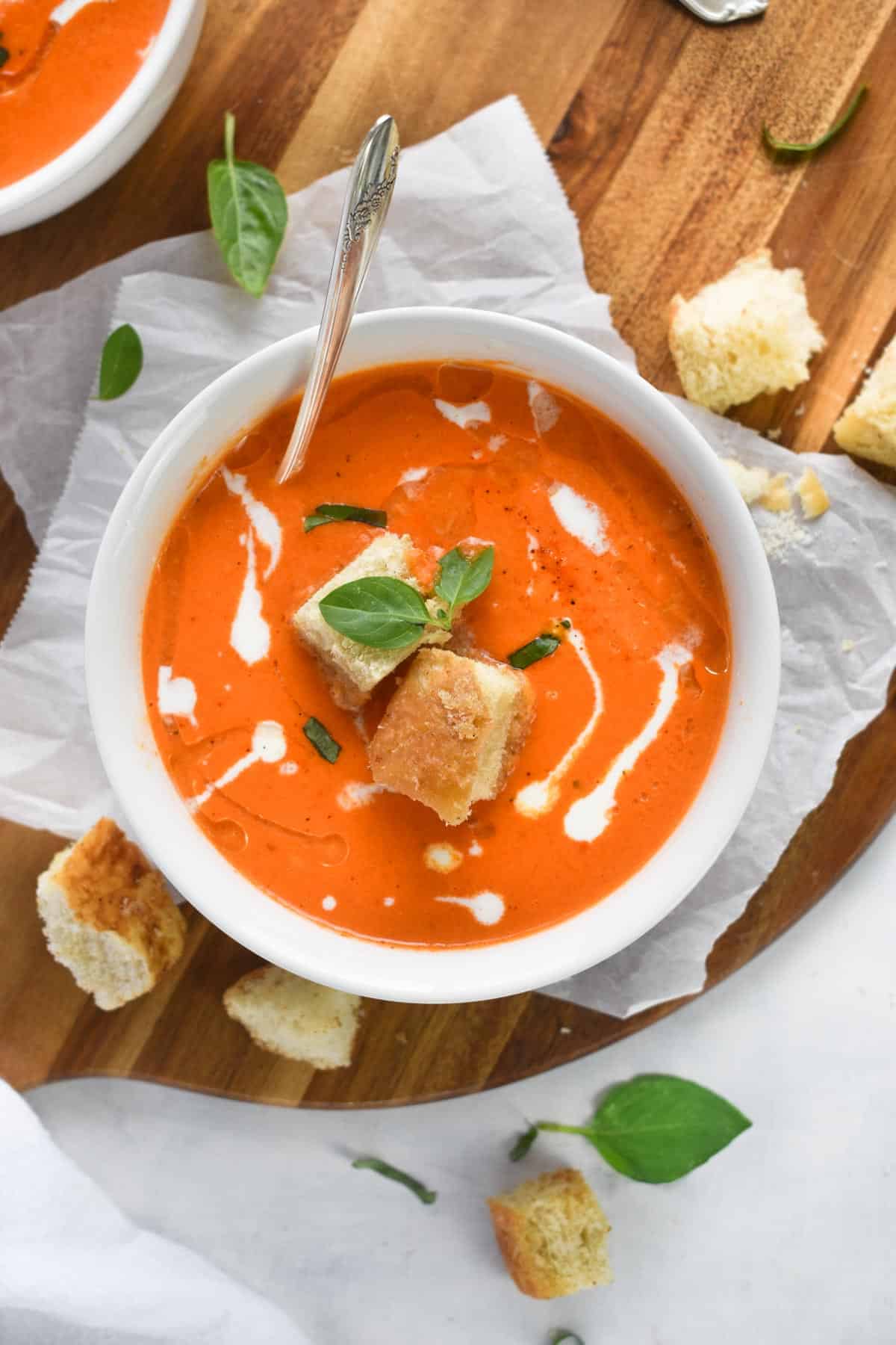 bowl of soup with spoon in it and croutons on side. 