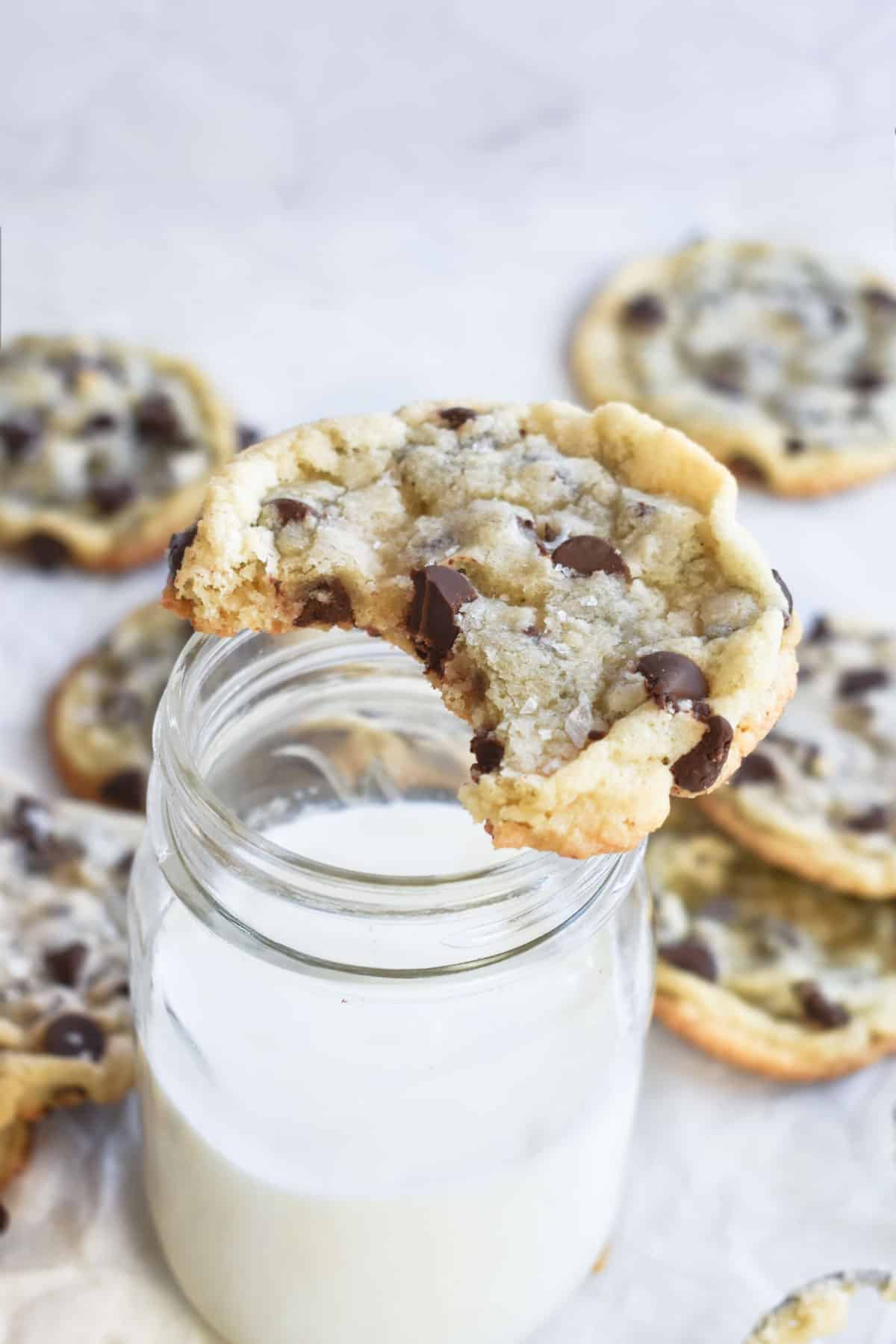 chocolate chip cookie without brown sugar with bite out of it on jar of milk. 