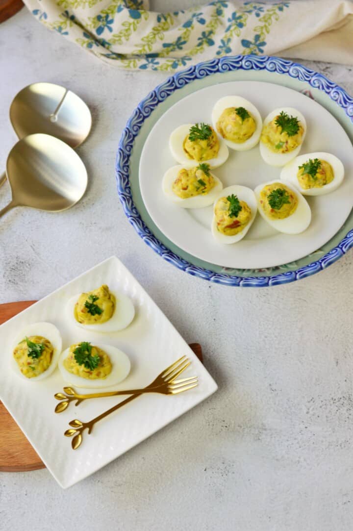 overhead picture of deviled eggs on blue and white platters with silver serving pieces.