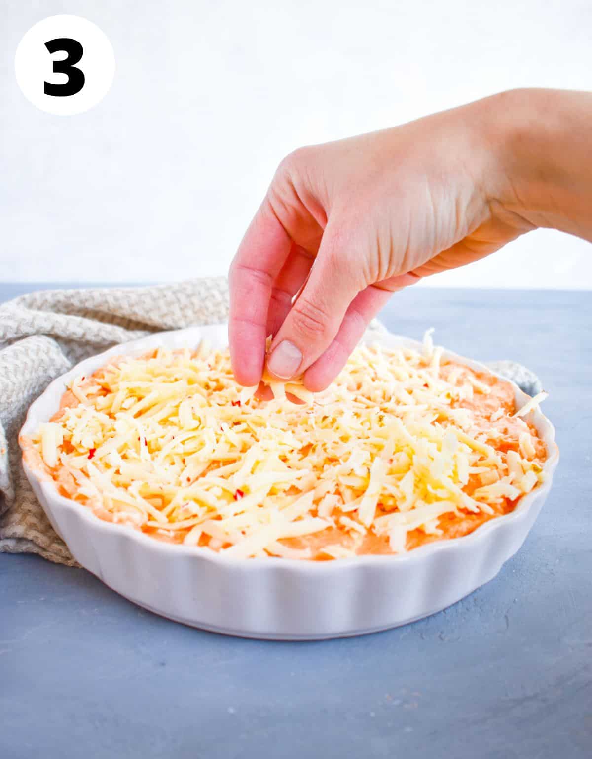 hand sprinkling cheese over top of dip. 