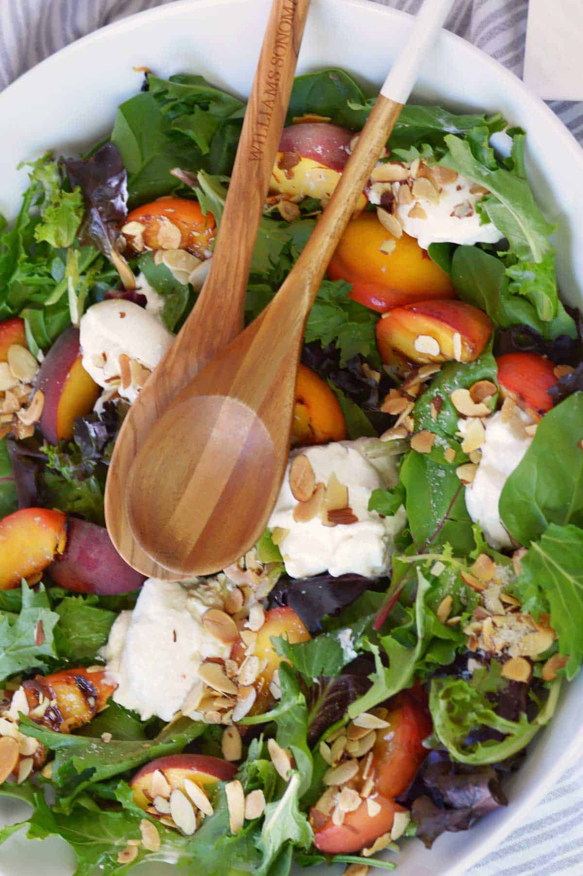 large salad bowl with grilled peach salad and wooden spoons.