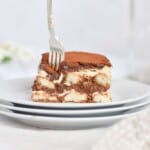 fork going into a slice of tiramisu on white plate.