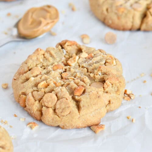 peanut butter cookie on parchment paper with chopped peanuts around it.