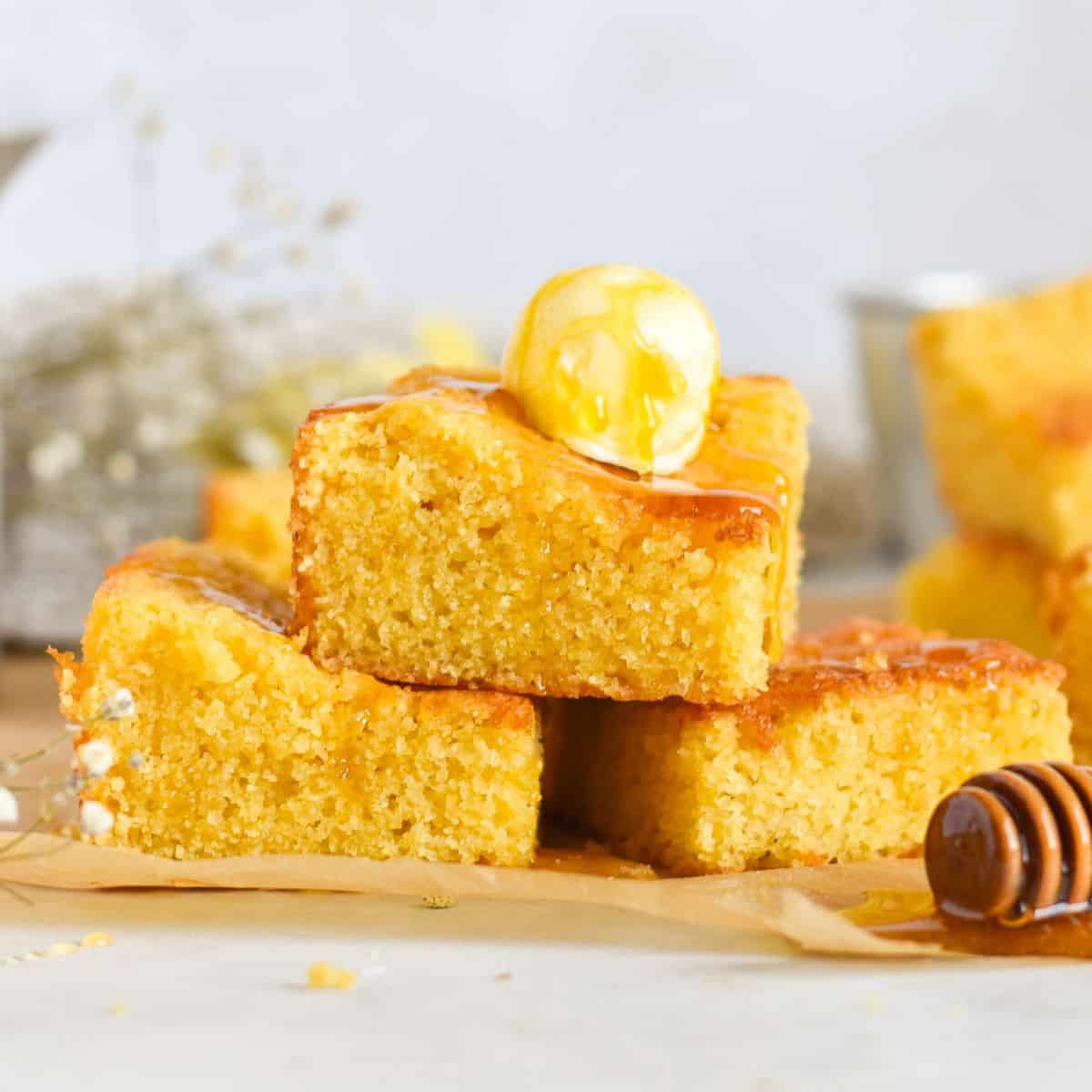 cornbread stacked on top of each other with butter and honey on top.