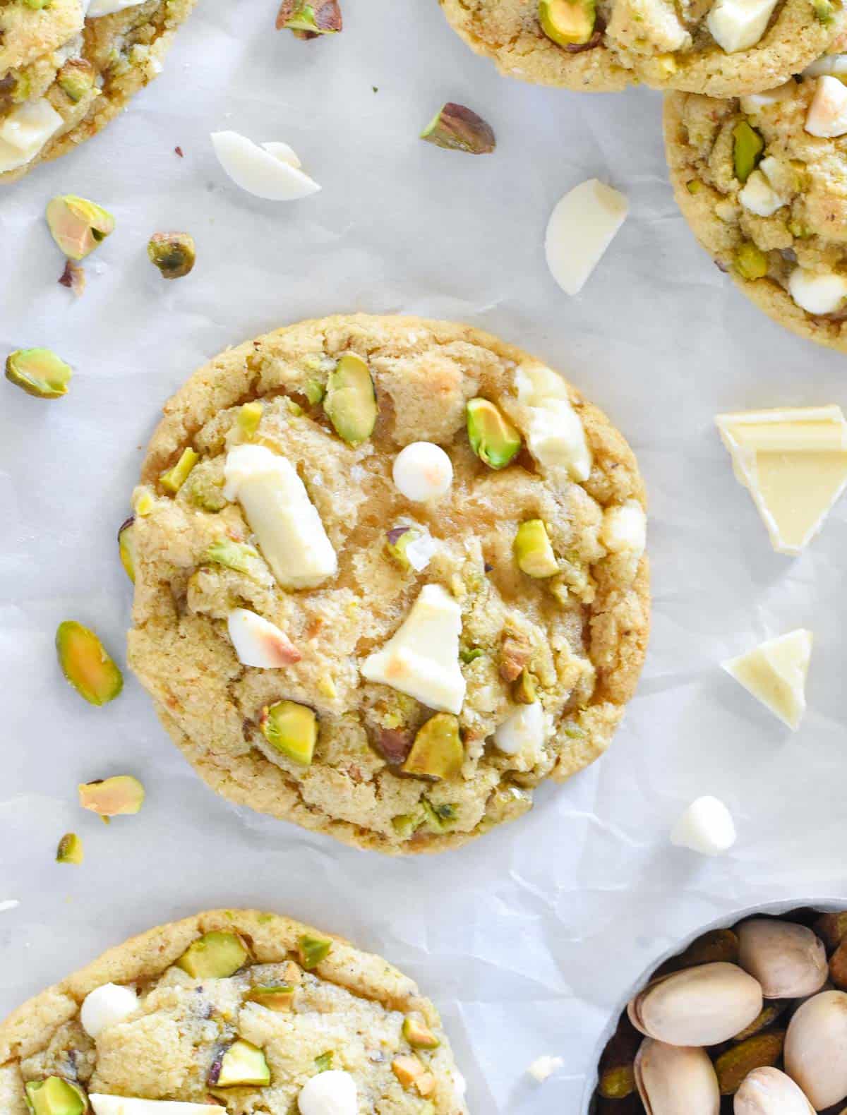 pistachio cookie with white chocolate chunks with nuts scattered around.